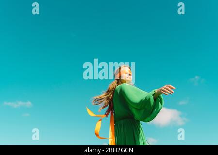 Junge Frau mit verbundenen Augen in einem grünen Kleid unter blauem Himmel Stockfoto