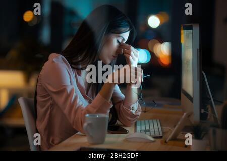 Müde junge Frau mit geschlossenen Augen sitzt am Schreibtisch im Büro Stockfoto