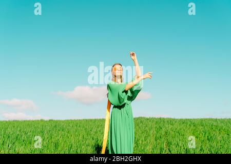 Junge Frau mit verbundenen Augen in einem grünen Kleid auf einem Feld stehend Stockfoto