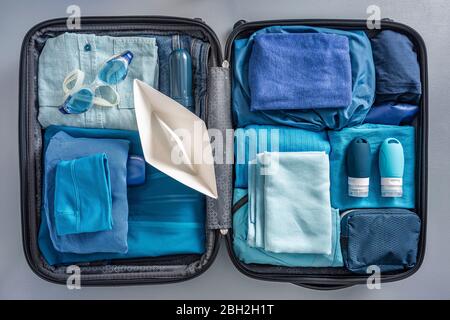 Ansicht von oben auf verpackten Koffer mit Kleidung, Schwimmbrille und Papierboot Stockfoto