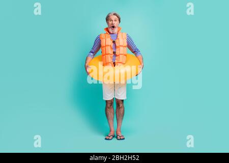 In voller Länge Foto von lustigen verrückt gealterten Seemann Schwimmer stehen innerhalb Kreis Rettungsring tragen gestreiften Seemann Hemd weiß Shorts orange Rettungsweste Flip-Flops Stockfoto