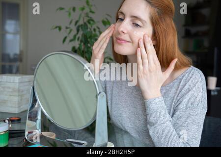 Junge Frau, die Gesichtscreme zu Hause anwendet Stockfoto