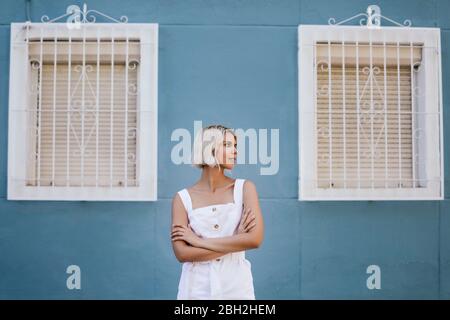 Porträt einer jungen Frau in weißem Sommerkleid vor der blauen Fassade Stockfoto