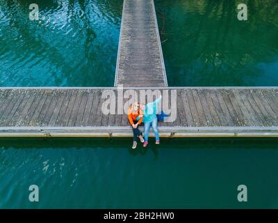 Zwei glückliche Freunde sitzen Seite an Seite auf dem Steg, Valdemurio Reservoir, Asturien, Spanien Stockfoto