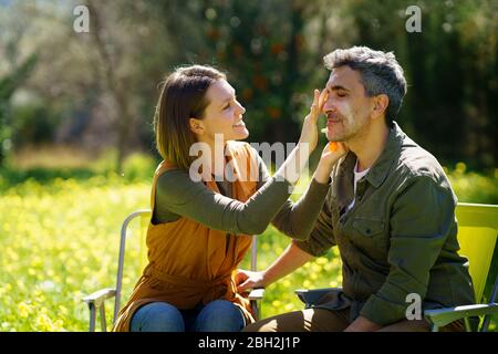 Junge Frau, die Sonnencreme auf ihren Freund auf dem Feld Stockfoto