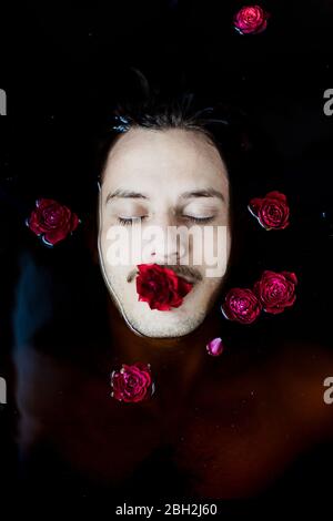 Porträt eines jungen Mannes mit roter Rose im Mund im Wasser schweben Stockfoto