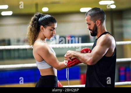 Trainer, der die Boxhandschuhe auf eine junge Boxerin legt Stockfoto