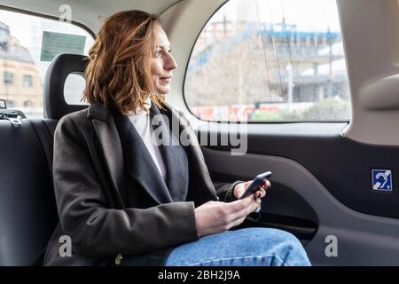 Geschäftsfrau im hinteren Teil eines Taxis, die aus dem Fenster schaut, London, Großbritannien Stockfoto