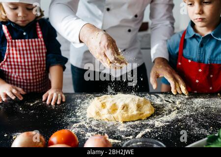 Vater mit zwei Kindern, die Teig für hausgemachte glutenfreie Pasta in der Küche zu Hause vorbereiten Stockfoto