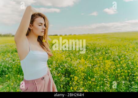 Junge Frau, die im Frühling auf einer Blumenwiese steht und im Mund blüht Stockfoto