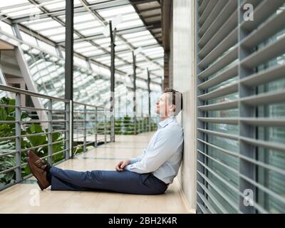 Geschäftsmann im grünen Atrium, auf der Galerie sitzend, denkend Stockfoto