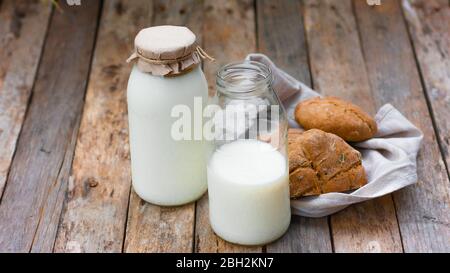 Eine Flasche frische Bio-Milch und rundes braunes Roggenflat auf einem rustikalen Holztisch. Gesundes Essen Konzept. Stockfoto