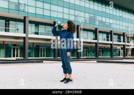 Sportliche junge Frau, die vor dem modernen Gebäude eine Abkühlung einschnüftt Stockfoto