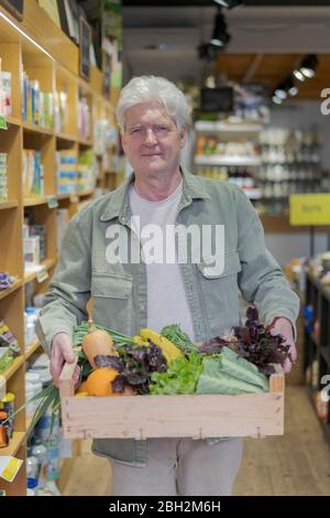 Porträt eines älteren Mannes, der eine Kiste mit Gemüse in einem kleinen Lebensmittelgeschäft trägt Stockfoto