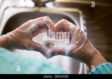Womans Hände gemacht Herzform mit seifigen Händen mit Waschbecken auf Hintergrund. Stockfoto