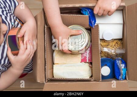 Kinder öffnen eine Lebensmittelzustellungsbox zu Hause, Online-Bestellung. Lieferung im Lebensmittelgeschäft. Box voller Lebensmittel in Konzept Spende Paket. Lieferung während Stockfoto