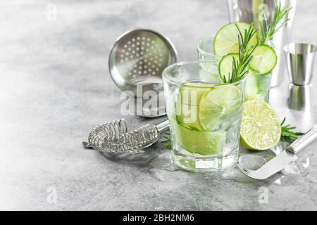 Bar-Accessoires und Zutaten für Cocktail-Drink mit Gurke, Limette, Rosmarin, Eis Stockfoto