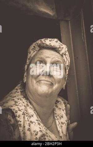 Vintage Sepia-Porträt der Hausfrau der 1940er Jahre, 1940 Frau, in Overalls und Kopftuch, aus dem Tierheim treten, Gesicht nach oben schauen, Kriegsnachstellung im Zweiten Weltkrieg. Stockfoto