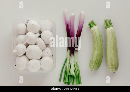 Frische Champignons weiße Champignons in Kunststoffverpackung und grüne Zwiebeln Schalotten oder Seelöwen auf weißem Hintergrund. Stockfoto