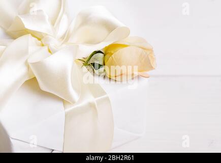 Geschenk mit einer schönen Satin große Schleife und Band und cremerosa auf Holz weißen Tisch Stockfoto