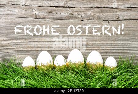 Osterdekoration. Ostereier im grünen Gras. Frohe Ostern deutscher Text Stockfoto
