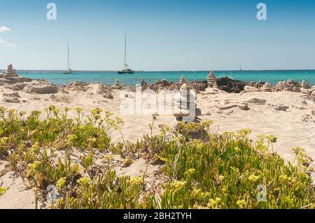 Nahaufnahme einer Steinpyramide in einem Sand- und Felsstrand. Im Hintergrund das Mittelmeer und Segelboote auf der Bucht. Formentera Spanien Stockfoto