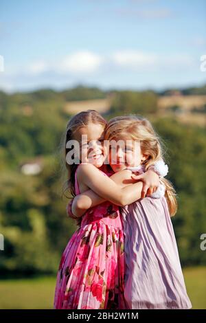 Junge Mädchen Zwillinge umarmen in Sonnenschein Stockfoto