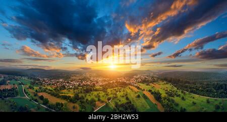 Luftpanorama einer weiten Landschaft mit einer kleinen Stadt bei einem wunderschönen bunten Sonnenuntergang mit dramatischem Himmel Stockfoto