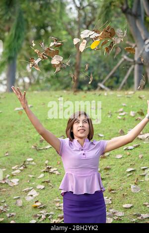 Portrait von Asean-Frau werfen trockene Blätter auf dem Rasen in einem Park. Stockfoto