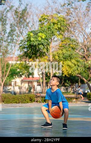 Asian Boy Holding ein Basketball Ball Hintergrund verschwommen Bäume. Stockfoto