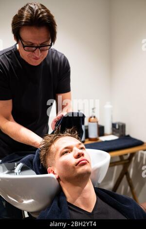 Barbier trocknet das gewaschene Haar eines jungen Mannes mit einem Handtuch in seinem Friseurladen. Stockfoto