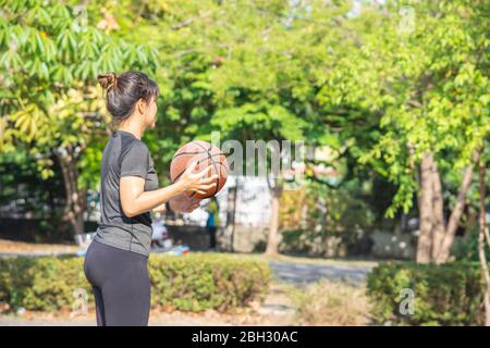 Basketball in der Hand asiatische Frau unscharfen Hintergrund Baum im Park. Stockfoto