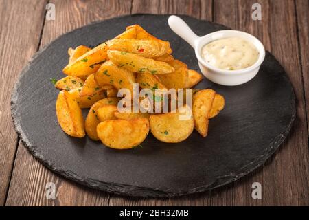 Gebratene Kartoffelspalten auf einem runden schwarzen Brett mit Senfsauce. Stockfoto