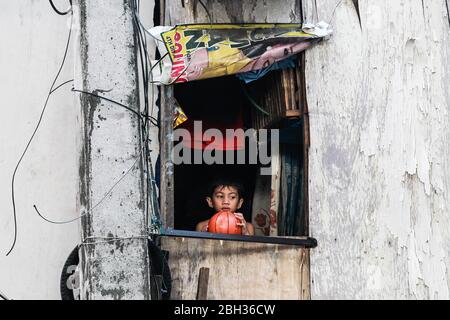 Quezon City. April 2020. Ein Junge hält seinen Ball, als er am 23. April 2020 aus dem Fenster seines Shanty auf ein Slum in Quezon City, Philippinen, blickt. Quelle: Rouelle Umali/Xinhua/Alamy Live News Stockfoto