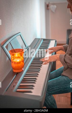 Hübsche Frau spielt zu Hause an beengten Tagen Klavier Stockfoto