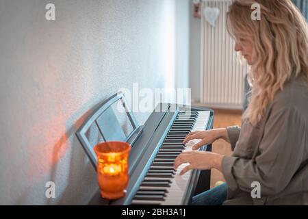 Hübsche Frau spielt zu Hause an beengten Tagen Klavier Stockfoto