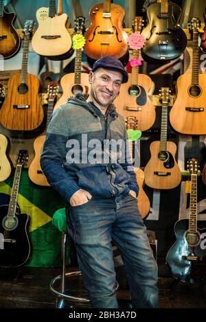 Besitzer Deicola Neves stolzer Gitarrenladenbesitzer posiert vor Instrumenten, die hinter ihm an der Wand hängen Stockfoto