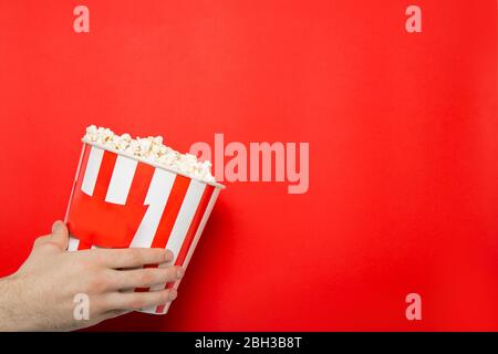 Der Kerl hält Popcorn in seinen Händen auf rotem Hintergrund. Platz für Text. Stockfoto