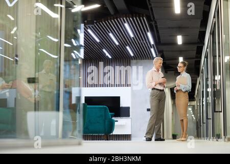 Zwei Geschäftsfrauen stehen und diskutieren miteinander, während sie in der modernen Halle des Bürogebäudes stehen Stockfoto