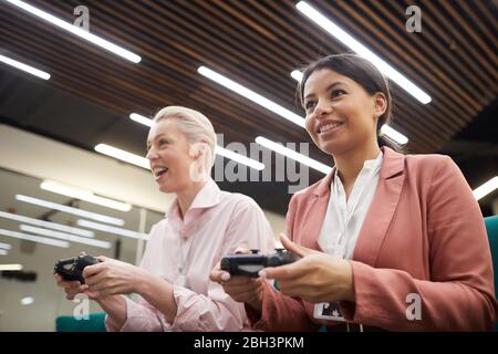 Zwei Geschäftsfrauen sitzen und spielen in Videospiel zusammen während der Pause im Büro Stockfoto