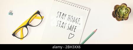 Worte bleiben zu Hause, bleiben Sie sicher in Notizbuch geschrieben, Konzept der Selbstquarantäne zu Hause als vorbeugende Virus Flat Lay Banner Stockfoto