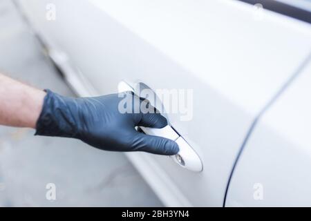 Fahrer mit chirurgischen Schutzhandschuhen, die die Autotür öffnen. Coronavirus-Prävention. Stockfoto