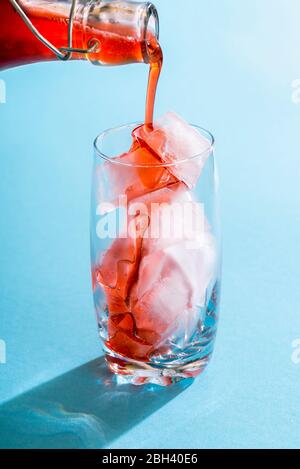 Erdbeersirup in ein Glas voller Eiswürfel gießen. Hausgemachter Erdbeersirup aus Bio-Früchten. Rote Früchte Sirup über Eiswürfel gießen A Stockfoto
