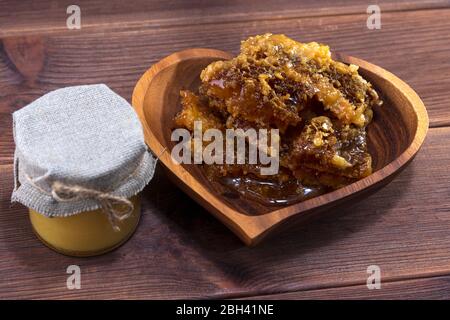 Glas mit Honig und eine Holzplatte mit Honig in Waben auf einem hölzernen Hintergrund Stockfoto