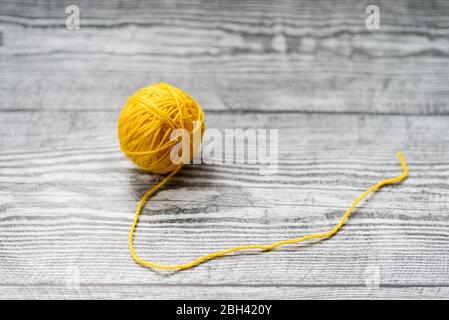 Eine Kugel aus gelber Wolle Stricknadeln auf dem hölzernen grauen Hintergrund. Stockfoto