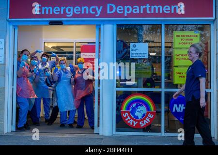 Southend-on-Sea, Großbritannien. 23. April 2020.Mitarbeiter des Gesundheitswesens am Southend University Hospital posieren am Eingang der Notaufnahme während eines Clap for Care Helfer Tributs in der COVID-19-Pandemie. Das Personal trägt persönliche Schutzausrüstung und gibt Daumen-nach-oben-Gesten unter Schildern, darunter „Notaufnahme“ und NHS-Regenbogenplakate, die die Sicherheit und den eingeschränkten Zugang fördern. Penelope Barritt/Alamy Live News Stockfoto