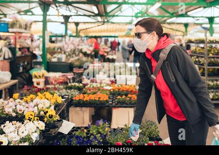 Frau mit einer Schutzmaske auf ihrem Gesicht Kauf frische Blumen auf einem lokalen Markt - Coronavirus Pandemie Zeit - flache Schärfentiefe Stockfoto