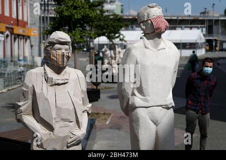 Lissabon, Portugal. April 2020. Ein Mann mit einer Gesichtsmaske geht an zwei Statuen vorbei, die ebenfalls mit Gesichtsmasken versehen sind, während die Ausbreitung der COVID-19 Coronavirus-Krankheit am 23. April 2020 in Lissabon, Portugal, andauert. Mit 820 Toten und 22353 bestätigten Fällen spürt das Land die Auswirkungen der COVID-19 Coronavirus-Pandemie. Kredit: Pedro Fiuza/ZUMA Wire/Alamy Live News Stockfoto