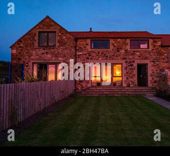 East Lothian, Schottland, Großbritannien. April 2020. UK Wetter: Ein atemberaubender, farbenprächtiger Sonnenuntergang in Orange spiegelt sich in den Fenstern eines Hauses in der Dämmerung Stockfoto