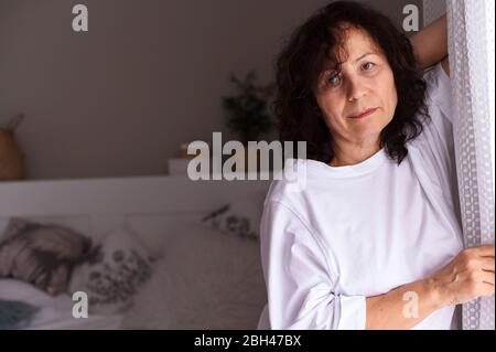 Eine Person, die für die Kamera posiert. Porträt einer Frau Senioren in weißen Kleidern, steht sie am Fenster und ist traurig. Kopierbereich. Soft-Fokus . Stockfoto